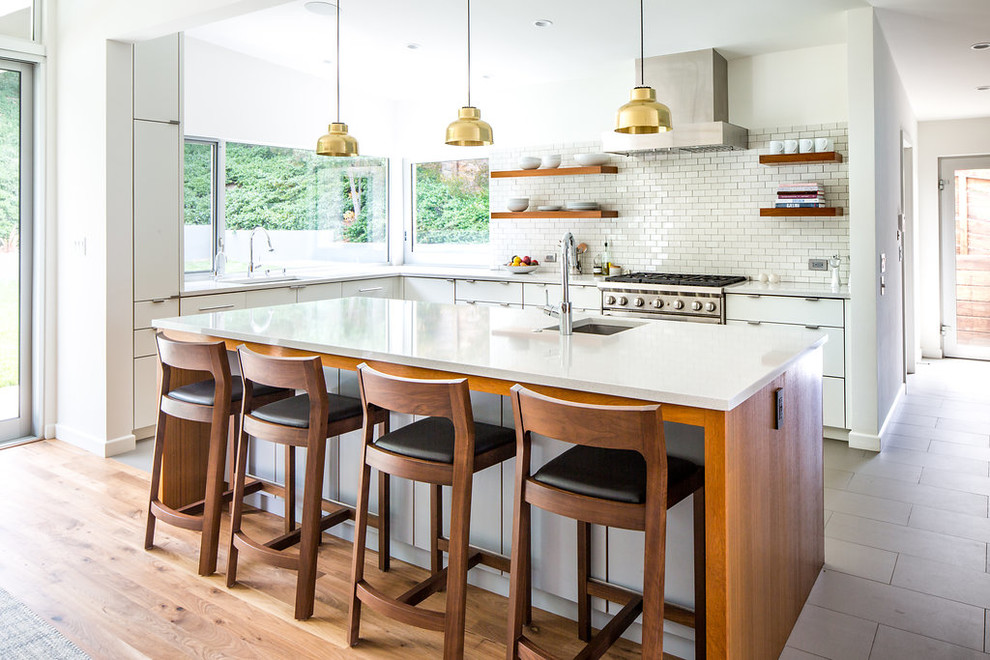 Example of a 1950s l-shaped porcelain tile and gray floor eat-in kitchen design in Los Angeles with an undermount sink, flat-panel cabinets, white cabinets, quartz countertops, white backsplash, ceramic backsplash, stainless steel appliances, an island and white countertops
