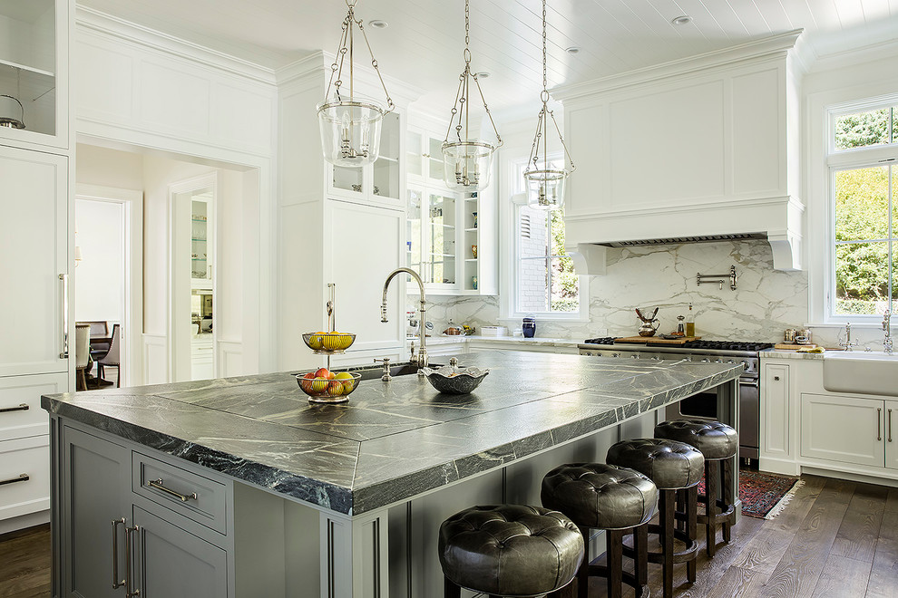 Example of a classic dark wood floor and brown floor enclosed kitchen design in Los Angeles with a farmhouse sink, shaker cabinets, white cabinets, marble countertops, white backsplash, marble backsplash, stainless steel appliances, an island and white countertops