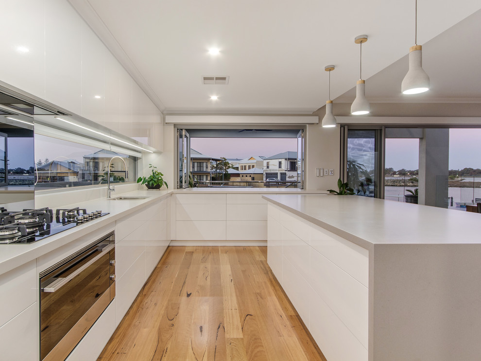 Moderne Wohnküche in U-Form mit Unterbauwaschbecken, flächenbündigen Schrankfronten, weißen Schränken, Rückwand-Fenster, schwarzen Elektrogeräten, braunem Holzboden, Kücheninsel, beigem Boden und grauer Arbeitsplatte in Perth