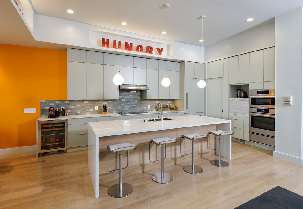 This is an example of a contemporary l-shaped kitchen/diner in San Francisco with a double-bowl sink, flat-panel cabinets, grey cabinets, grey splashback, stainless steel appliances, light hardwood flooring and an island.