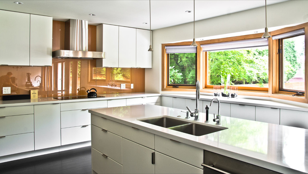 Cette image montre une cuisine minimaliste avec un évier encastré, un placard à porte plane, des portes de placard blanches, une crédence orange et une crédence en feuille de verre.