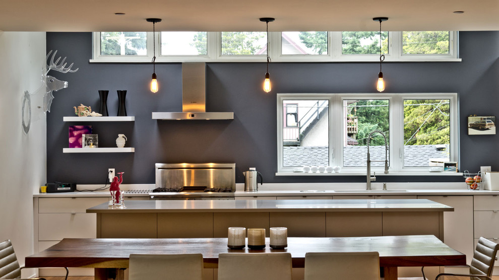 Idées déco pour une cuisine américaine linéaire moderne avec un électroménager en acier inoxydable, un placard à porte plane et des portes de placard blanches.