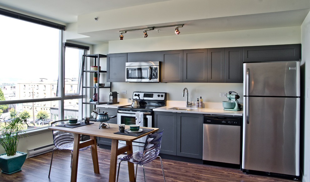 На фото: прямая кухня в современном стиле с техникой из нержавеющей стали, серыми фасадами и обеденным столом