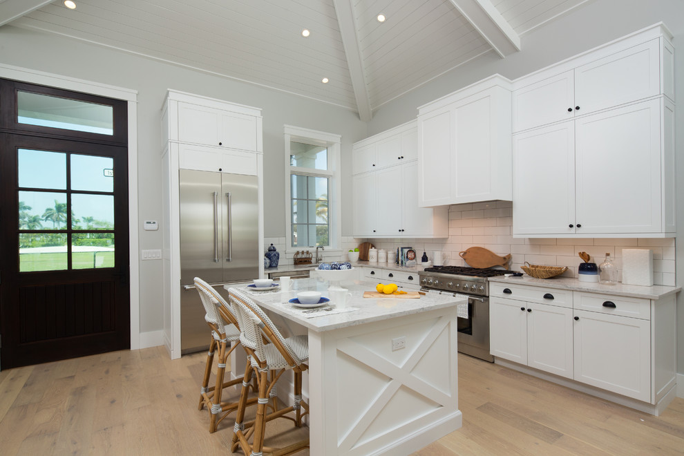 Beach style l-shaped kitchen in Miami with a double-bowl sink, shaker cabinets, white cabinets, soapstone worktops, white splashback, metro tiled splashback, stainless steel appliances, an island and medium hardwood flooring.