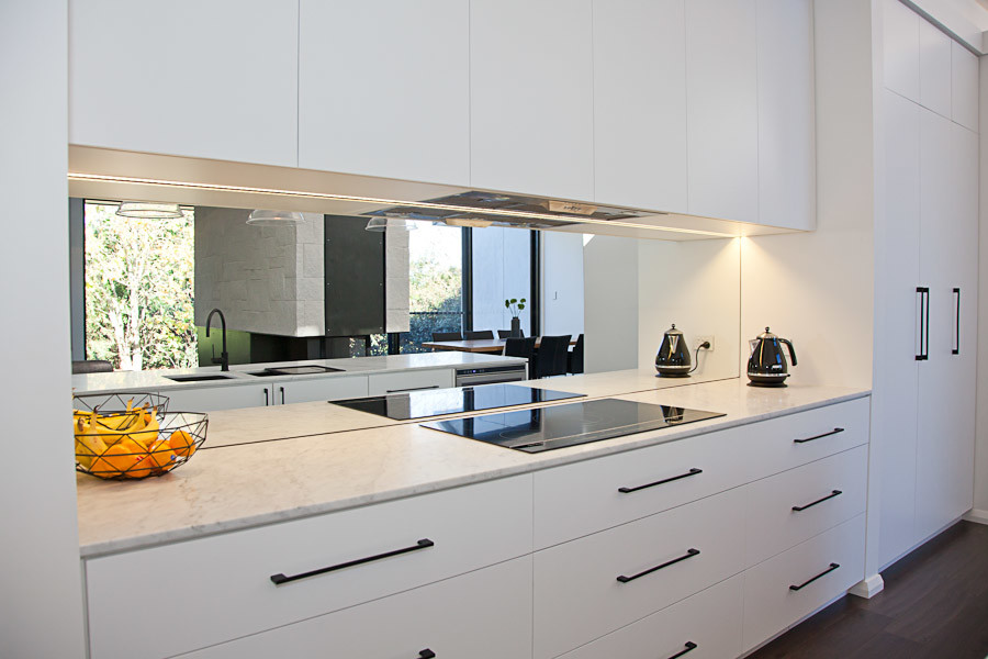 Idéer för ett stort modernt kök, med en undermonterad diskho, släta luckor, vita skåp, marmorbänkskiva, spegel som stänkskydd och en köksö