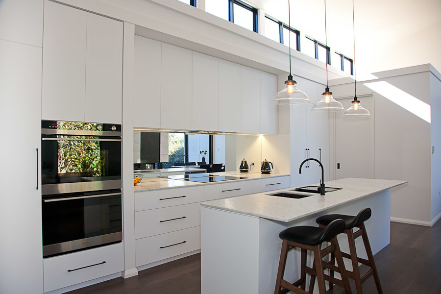 Inredning av ett modernt stort kök, med en undermonterad diskho, släta luckor, vita skåp, marmorbänkskiva, spegel som stänkskydd och en köksö
