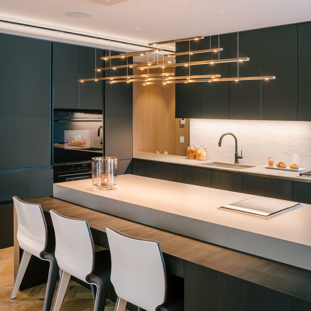 Large minimalist single-wall light wood floor and beige floor open concept kitchen photo in New York with an undermount sink, flat-panel cabinets, black cabinets, concrete countertops, gray backsplash, stone slab backsplash, black appliances and an island