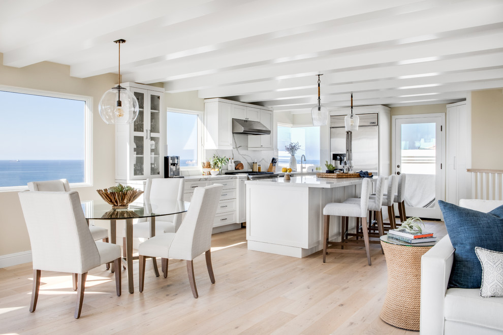 This is an example of a medium sized nautical kitchen/diner in Los Angeles with shaker cabinets, white cabinets, marble worktops, white splashback, marble splashback, light hardwood flooring, an island and white worktops.