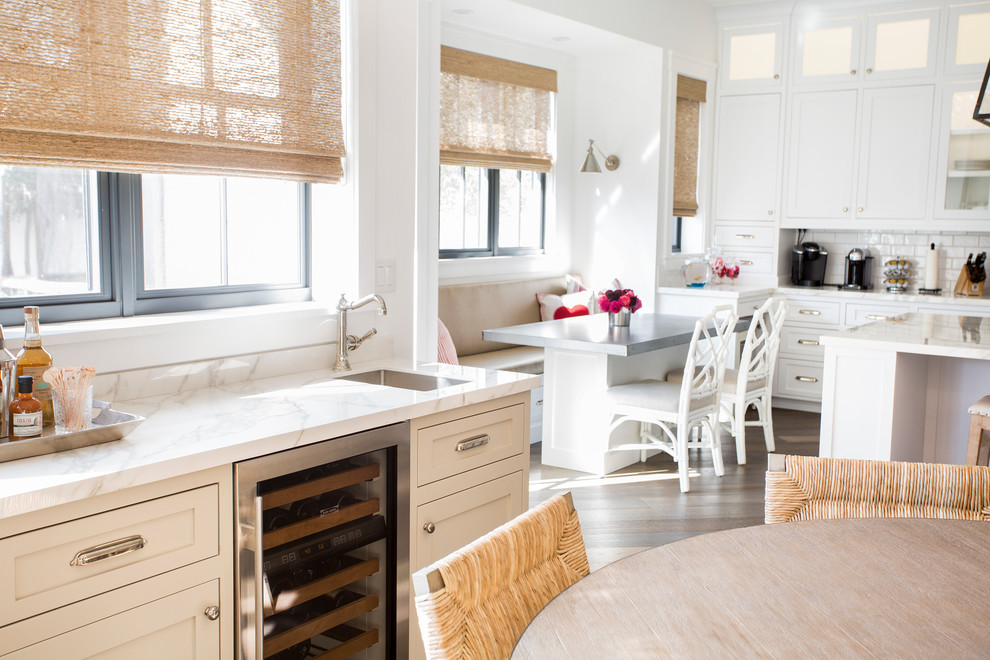 Foto på ett maritimt kök och matrum, med skåp i mellenmörkt trä, vitt stänkskydd, stänkskydd i porslinskakel, rostfria vitvaror, mellanmörkt trägolv, en köksö och brunt golv