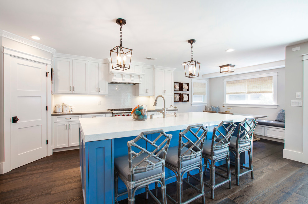 This is an example of a nautical galley kitchen in Los Angeles with shaker cabinets, white cabinets, white splashback, stainless steel appliances, dark hardwood flooring and an island.