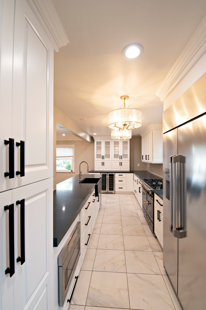 Large traditional galley kitchen/diner in San Diego with a belfast sink, raised-panel cabinets, white cabinets, engineered stone countertops, white splashback, porcelain splashback, stainless steel appliances, porcelain flooring, no island, white floors and grey worktops.