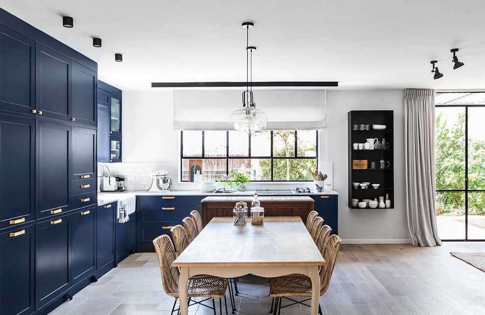 Example of a large classic l-shaped light wood floor eat-in kitchen design in Los Angeles with a farmhouse sink, recessed-panel cabinets, blue cabinets, quartz countertops, white backsplash, ceramic backsplash, stainless steel appliances and white countertops