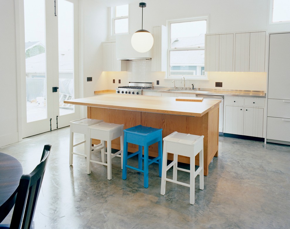 Идея дизайна: прямая кухня в морском стиле с обеденным столом, белыми фасадами, деревянной столешницей, белым фартуком, техникой из нержавеющей стали, бетонным полом и островом