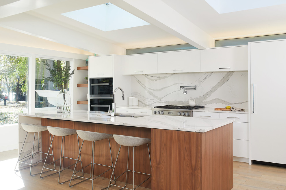 Zweizeilige, Große Moderne Wohnküche mit flächenbündigen Schrankfronten, weißen Schränken, Küchengeräten aus Edelstahl, hellem Holzboden, Kücheninsel, weißer Arbeitsplatte, weißem Boden, Küchenrückwand in Weiß und Rückwand aus Marmor in Los Angeles