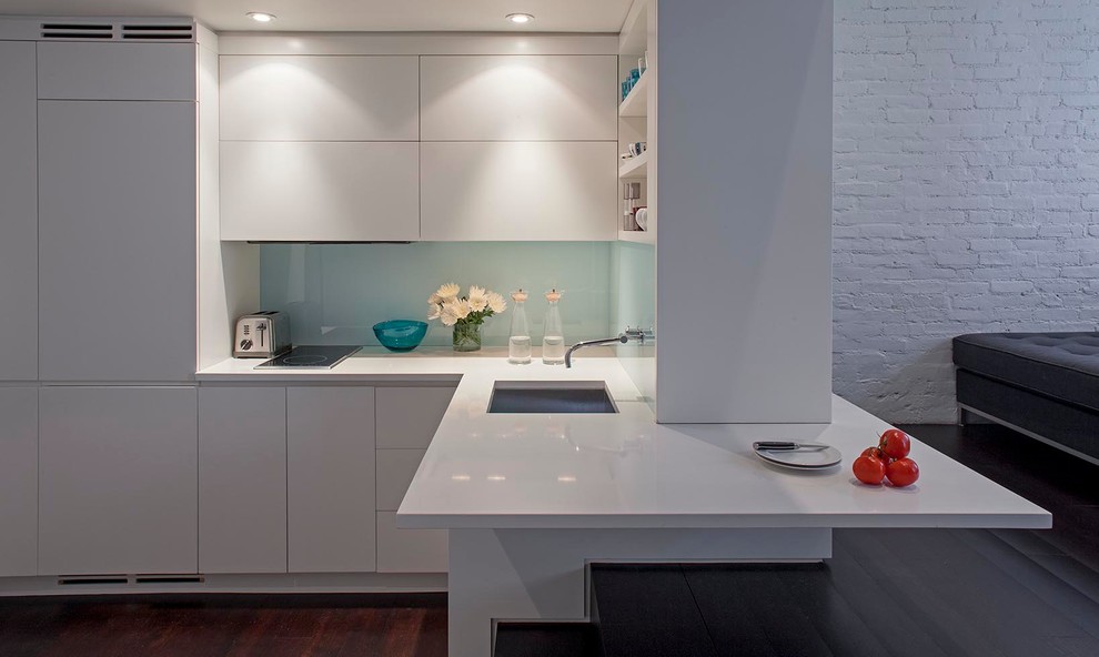 Exempel på ett litet modernt kök, med vita skåp, glaspanel som stänkskydd, rostfria vitvaror, mörkt trägolv, en undermonterad diskho, släta luckor, vitt stänkskydd och en halv köksö
