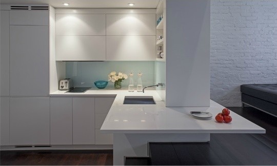 Design ideas for a small modern l-shaped kitchen in New York with white cabinets, glass sheet splashback, stainless steel appliances, dark hardwood flooring, a submerged sink, flat-panel cabinets, white splashback and a breakfast bar.