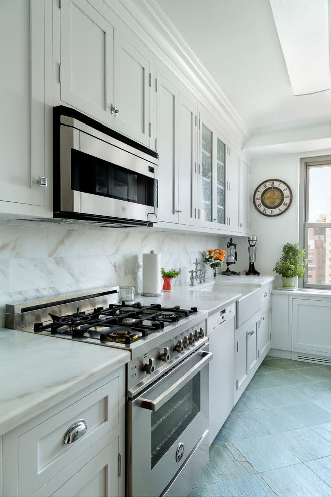 Photo of a small classic galley enclosed kitchen in New York with a belfast sink, recessed-panel cabinets, white cabinets, marble worktops, white splashback, stone tiled splashback, stainless steel appliances, slate flooring and no island.