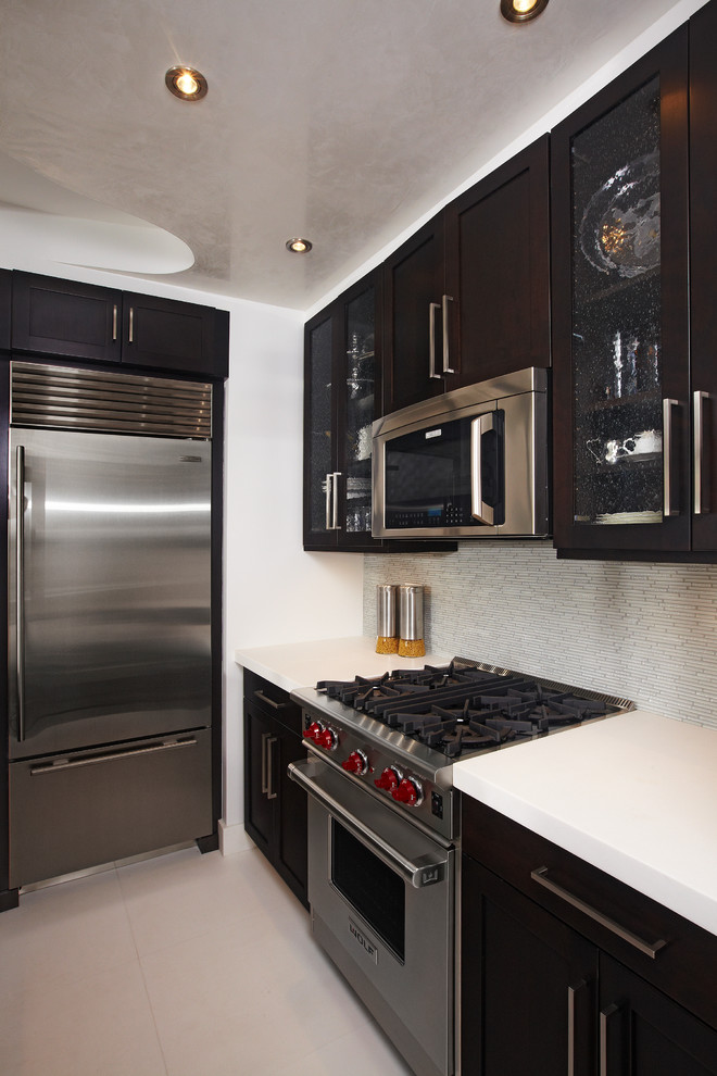 Example of a small trendy single-wall dark wood floor open concept kitchen design in New York with black cabinets, stainless steel appliances, no island, an undermount sink, glass-front cabinets, solid surface countertops, white backsplash and matchstick tile backsplash