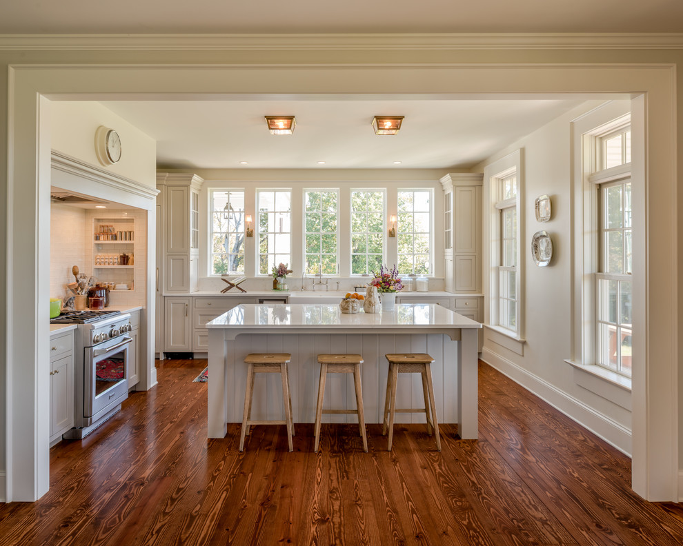 Example of a cottage dark wood floor and brown floor kitchen design in Philadelphia with a farmhouse sink, shaker cabinets, beige cabinets, stainless steel appliances and an island