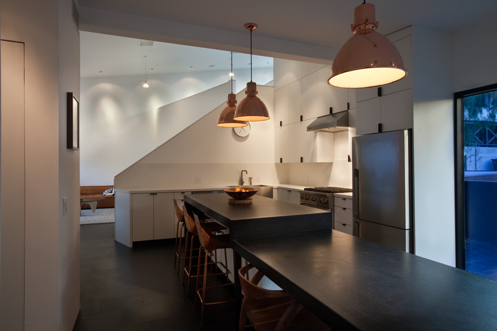 This is an example of a small contemporary l-shaped open plan kitchen in Los Angeles with a belfast sink, flat-panel cabinets, white cabinets, granite worktops, white splashback, stone slab splashback, stainless steel appliances, porcelain flooring, an island and black floors.