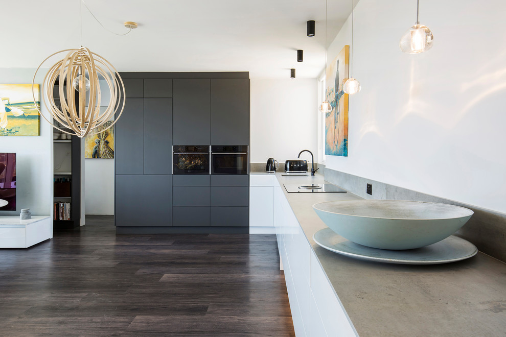 Large scandi grey and white l-shaped open plan kitchen in Sydney with a submerged sink, flat-panel cabinets, black appliances, no island, brown floors, grey worktops, grey cabinets and engineered stone countertops.