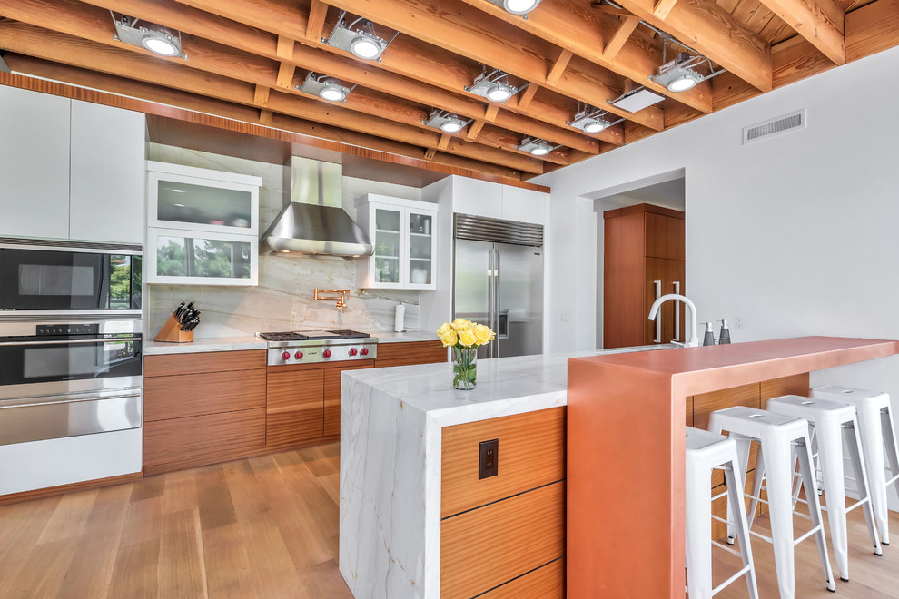 Photo of a contemporary galley kitchen in Phoenix with a submerged sink, flat-panel cabinets, medium wood cabinets, white splashback, stainless steel appliances, medium hardwood flooring, a breakfast bar and brown floors.