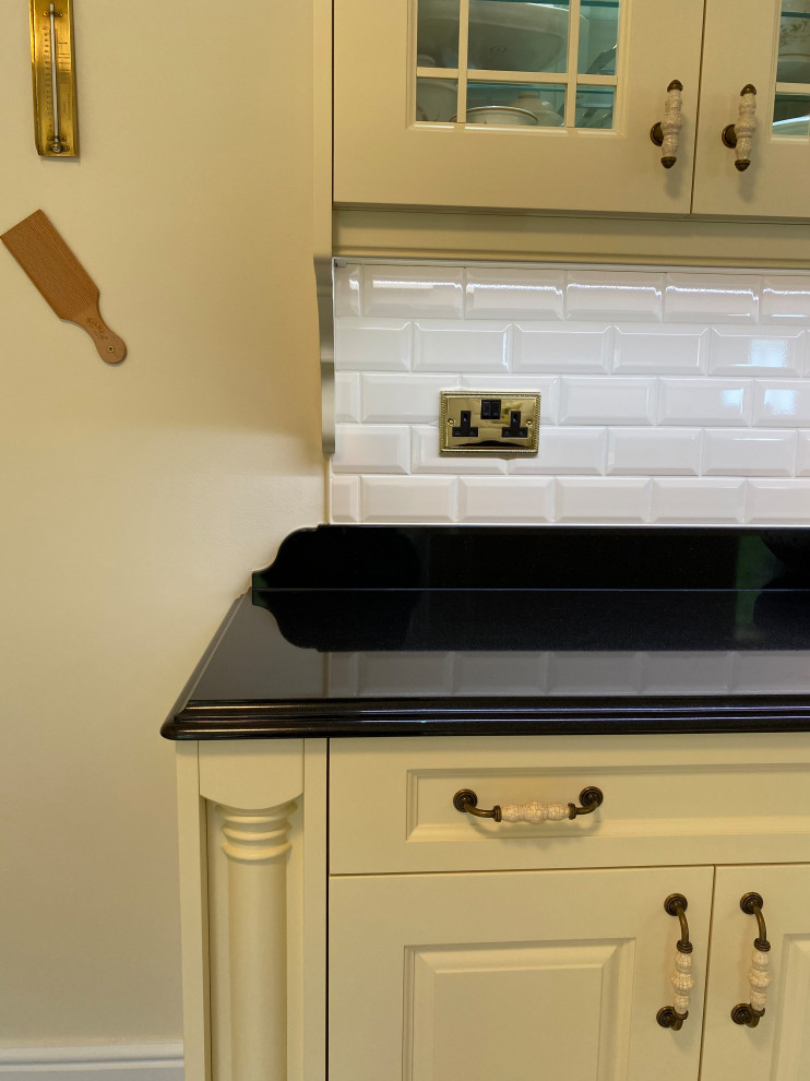 Idéer för att renovera ett stort vintage svart svart kök, med en rustik diskho, luckor med upphöjd panel, vita skåp, granitbänkskiva, svart stänkskydd, integrerade vitvaror, klinkergolv i keramik, en köksö och flerfärgat golv