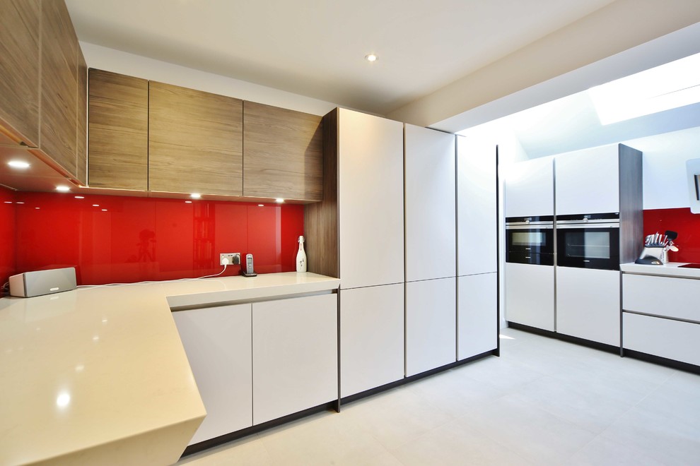 Large contemporary galley open plan kitchen in London with flat-panel cabinets, medium wood cabinets, quartz worktops, red splashback, glass sheet splashback, stainless steel appliances and a breakfast bar.