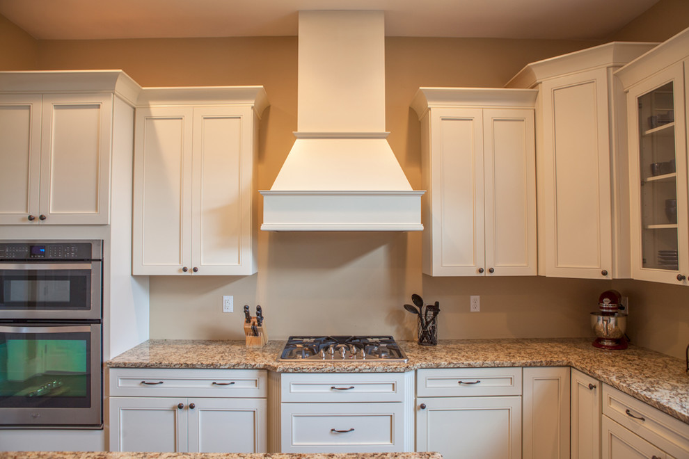 Foto på ett avskilt, mellanstort vintage l-kök, med en undermonterad diskho, luckor med infälld panel, vita skåp, granitbänkskiva, rostfria vitvaror, mellanmörkt trägolv, en köksö och brunt golv