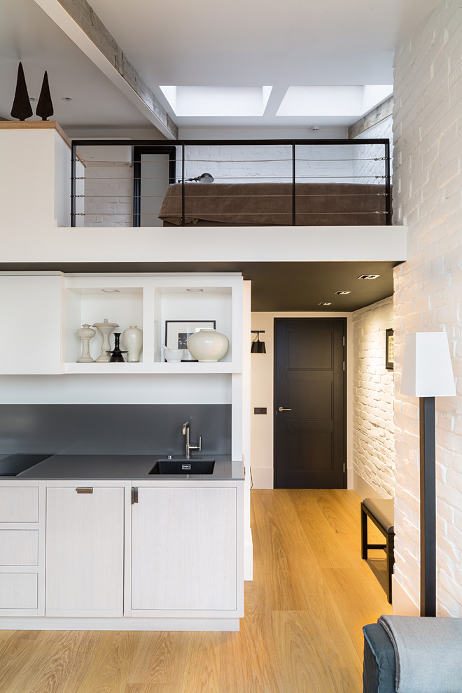 This is an example of a small urban single-wall open plan kitchen in Moscow with a submerged sink, flat-panel cabinets, light wood cabinets, quartz worktops, grey splashback, light hardwood flooring and no island.
