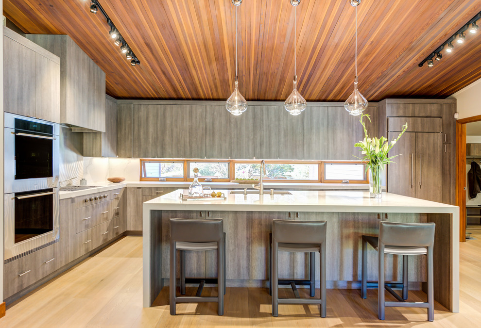 Large contemporary l-shaped kitchen in San Francisco with flat-panel cabinets, engineered stone countertops, light hardwood flooring, an island, beige floors, white worktops, light wood cabinets, window splashback and integrated appliances.