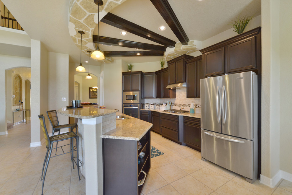 Large transitional galley ceramic tile and beige floor open concept kitchen photo in Austin with a double-bowl sink, raised-panel cabinets, dark wood cabinets, granite countertops, white backsplash, stone tile backsplash, stainless steel appliances and an island