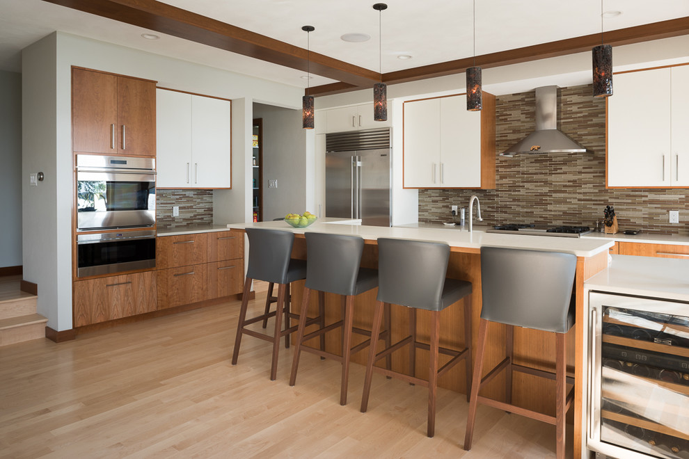 Foto på ett funkis kök med öppen planlösning, med släta luckor, vita skåp, flerfärgad stänkskydd, stänkskydd i glaskakel, rostfria vitvaror, ljust trägolv och en köksö