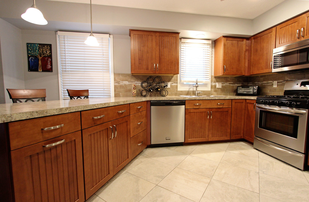 Example of a mid-sized l-shaped eat-in kitchen design in Cleveland with recessed-panel cabinets, medium tone wood cabinets, laminate countertops, beige backsplash, stone tile backsplash, stainless steel appliances and a peninsula