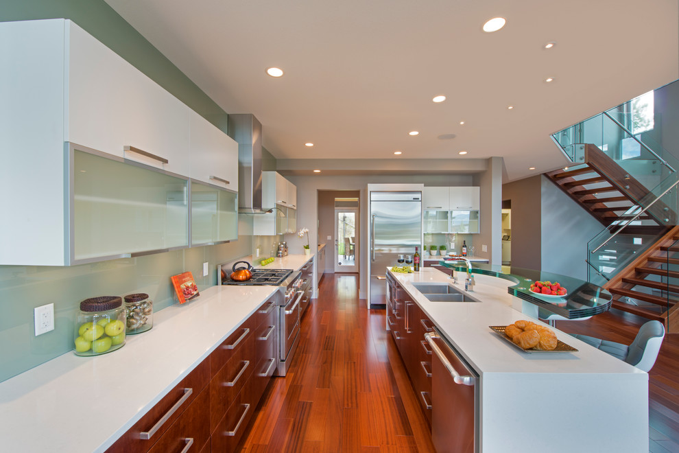 Mittelgroße Moderne Wohnküche in L-Form mit flächenbündigen Schrankfronten, weißen Schränken, Küchenrückwand in Grün, Glasrückwand, Küchengeräten aus Edelstahl, hellem Holzboden und Kücheninsel in Vancouver