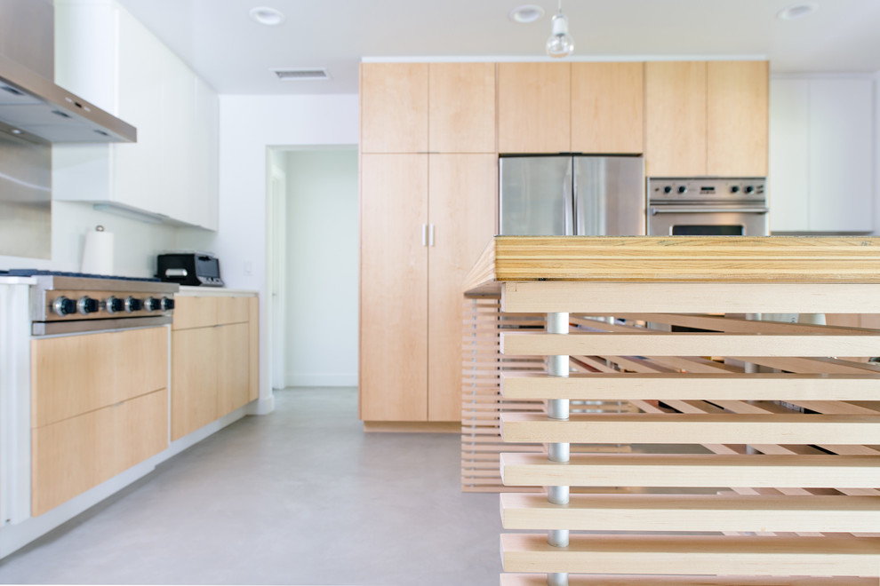 Inredning av ett modernt stort kök, med skåp i ljust trä, vitt stänkskydd, rostfria vitvaror, betonggolv, en köksö, släta luckor, träbänkskiva och en undermonterad diskho
