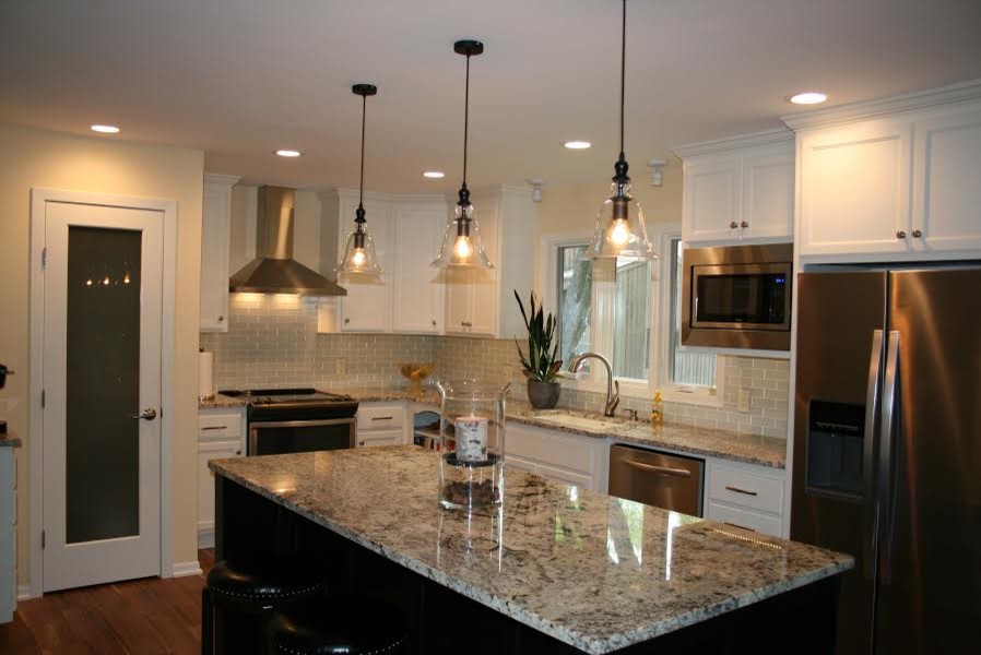 Inredning av ett modernt kök, med en undermonterad diskho, skåp i shakerstil, vita skåp, granitbänkskiva, grått stänkskydd, stänkskydd i glaskakel, rostfria vitvaror, mörkt trägolv och en köksö