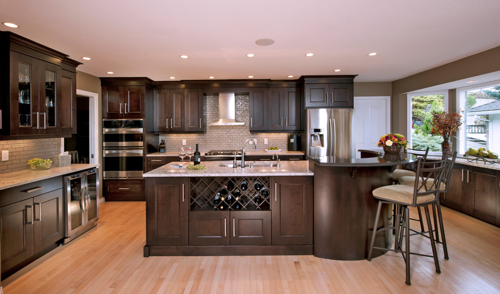 Large u-shaped kitchen/diner in Vancouver with a submerged sink, recessed-panel cabinets, dark wood cabinets, glass tiled splashback, stainless steel appliances, light hardwood flooring and an island.