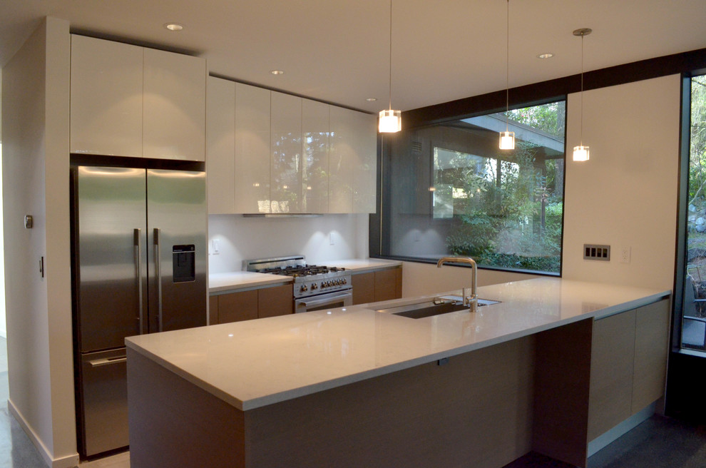 Пример оригинального дизайна: параллельная кухня-гостиная среднего размера в стиле модернизм с врезной мойкой, плоскими фасадами, белыми фасадами, столешницей из акрилового камня, белым фартуком и техникой из нержавеющей стали
