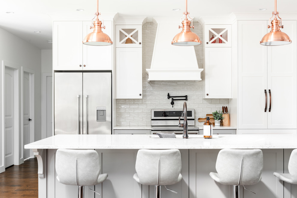 Foto på ett stort lantligt vit kök och matrum, med en undermonterad diskho, skåp i shakerstil, vita skåp, bänkskiva i kvarts, vitt stänkskydd, stänkskydd i porslinskakel, rostfria vitvaror, mellanmörkt trägolv, en köksö och brunt golv