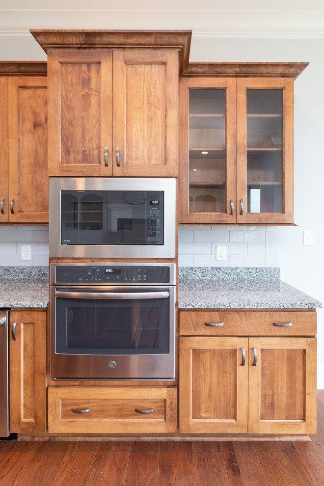 Foto på ett mellanstort vintage flerfärgad kök, med en integrerad diskho, släta luckor, bruna skåp, bänkskiva i kvarts, grått stänkskydd, stänkskydd i tunnelbanekakel, rostfria vitvaror, mellanmörkt trägolv, en köksö och brunt golv