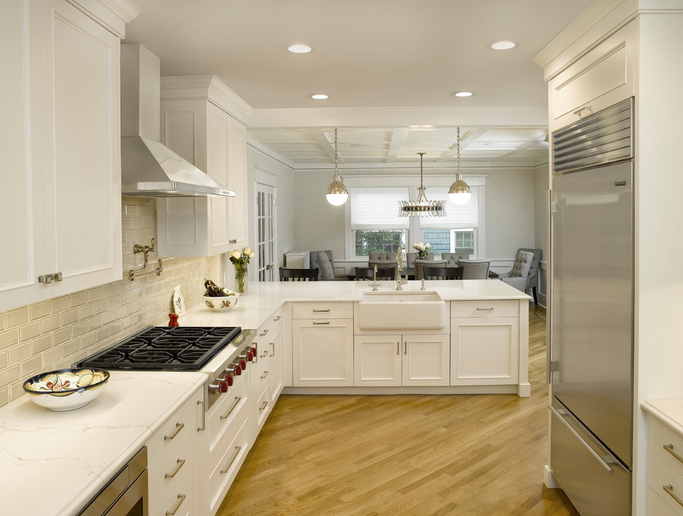 Eat-in kitchen - mid-sized transitional l-shaped medium tone wood floor and beige floor eat-in kitchen idea in New York with a farmhouse sink, flat-panel cabinets, white cabinets, quartz countertops, gray backsplash, ceramic backsplash, stainless steel appliances and a peninsula
