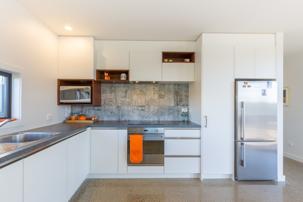 Foto di una cucina a L contemporanea con lavello da incasso, ante lisce, ante bianche, paraspruzzi grigio e elettrodomestici in acciaio inossidabile