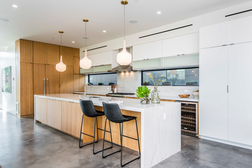 Contemporary open plan kitchen in Los Angeles with a submerged sink, flat-panel cabinets, white cabinets, white splashback, window splashback, stainless steel appliances, an island and grey floors.