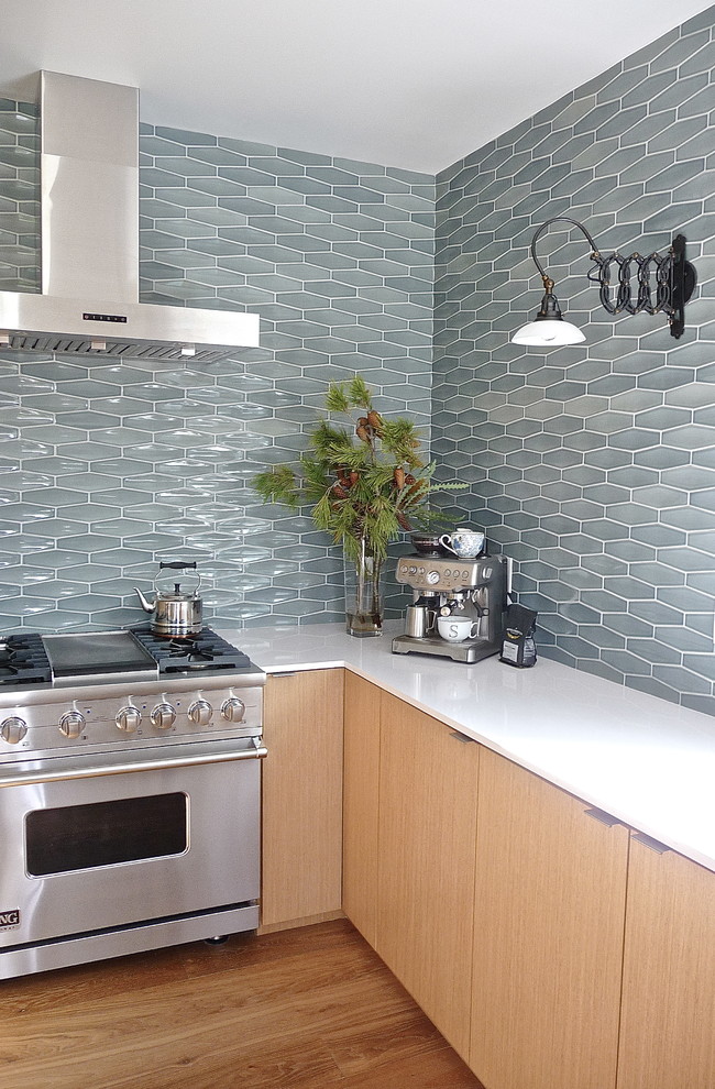 Moderne Küche mit braunem Holzboden, Küchengeräten aus Edelstahl, Rückwand aus Keramikfliesen, Küchenrückwand in Blau, hellen Holzschränken und flächenbündigen Schrankfronten in Sonstige
