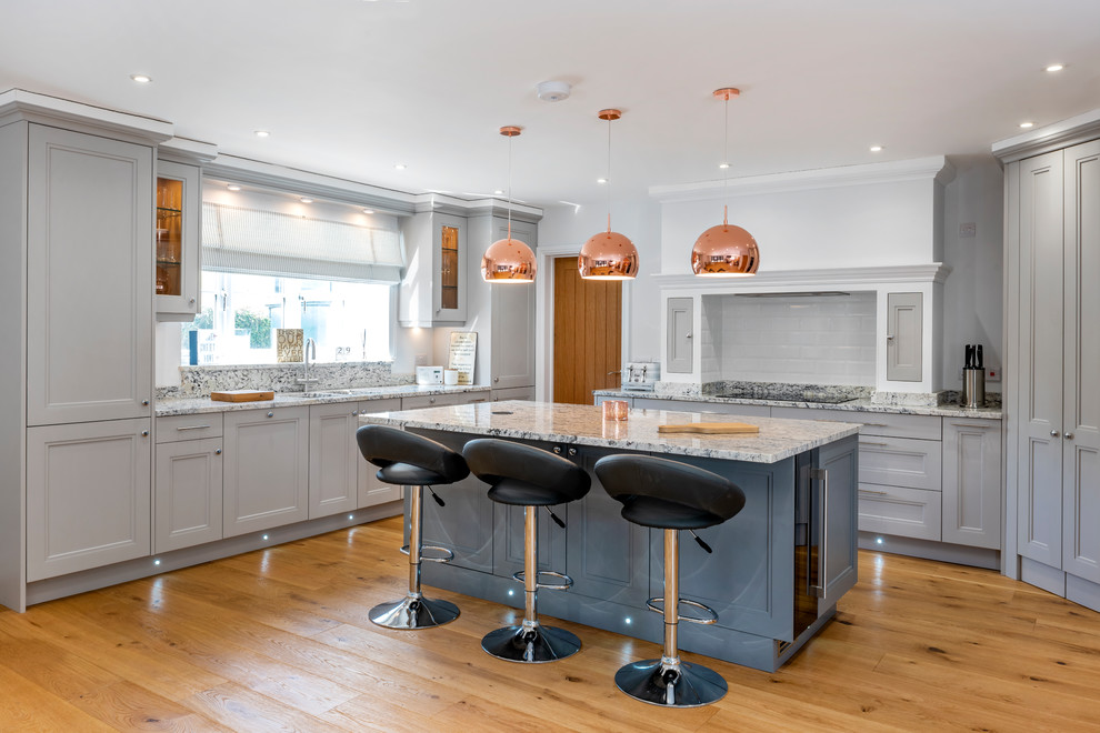 Large traditional kitchen in Other with recessed-panel cabinets, grey cabinets, marble worktops, white splashback, metro tiled splashback, an island, grey worktops and medium hardwood flooring.