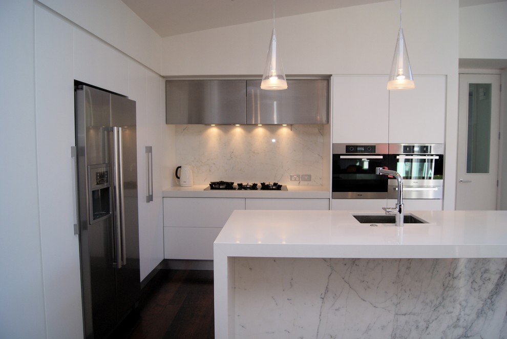 Foto på ett litet funkis kök, med rostfria vitvaror, en undermonterad diskho, mörkt trägolv, en köksö, släta luckor, vita skåp, bänkskiva i kvarts och stänkskydd i marmor