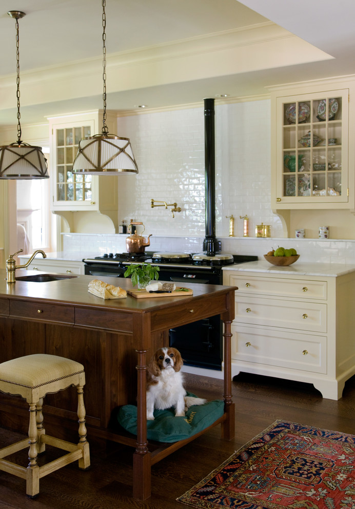 Ornate dark wood floor kitchen photo in Boston with yellow cabinets, marble countertops, white backsplash, subway tile backsplash, black appliances, an island, a single-bowl sink and glass-front cabinets