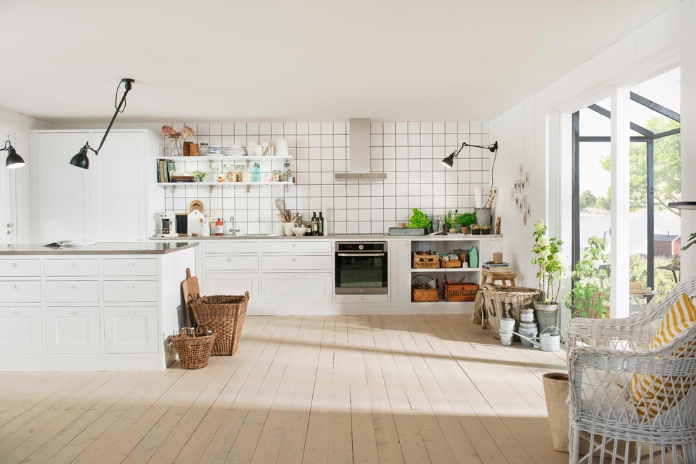 Inspiration för mellanstora nordiska kök, med en integrerad diskho, skåp i shakerstil, vita skåp, rostfria vitvaror, målat trägolv, en köksö, vitt stänkskydd och stänkskydd i porslinskakel