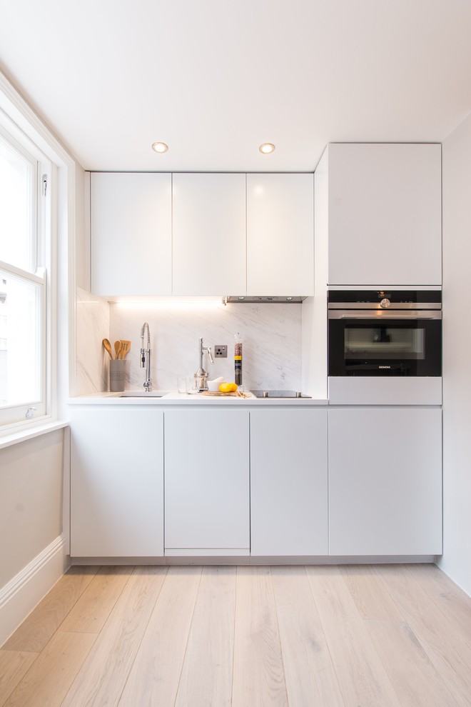 Inspiration for a small contemporary single-wall open plan kitchen in London with a single-bowl sink, flat-panel cabinets, white cabinets, composite countertops, white splashback, marble splashback, stainless steel appliances, medium hardwood flooring, no island and brown floors.